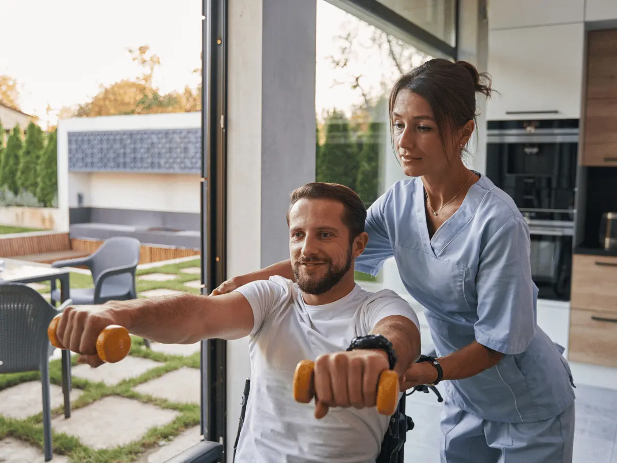 Disabled man in wheelchair lifting small arm weights with nurses help