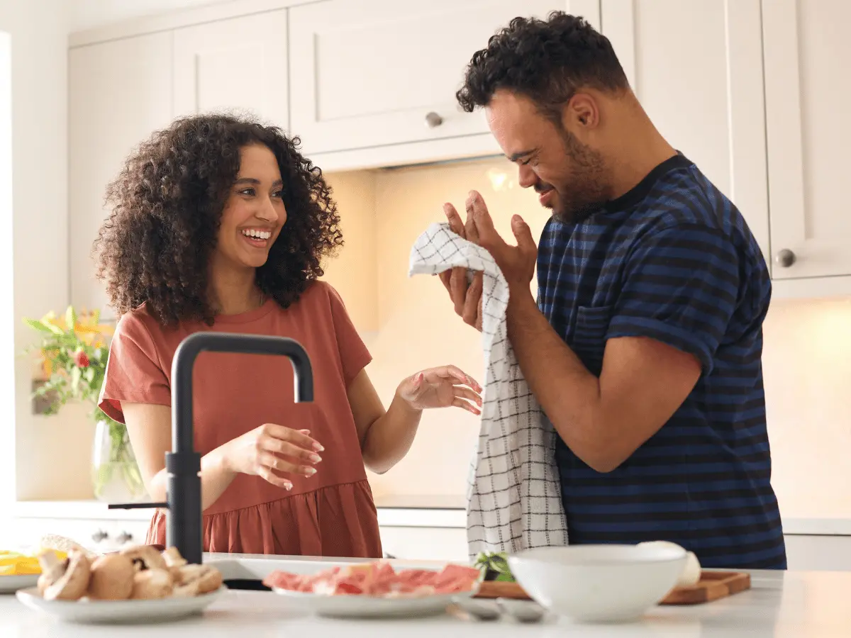 Man with down syndrome drying hands in the kitchen with help of carer